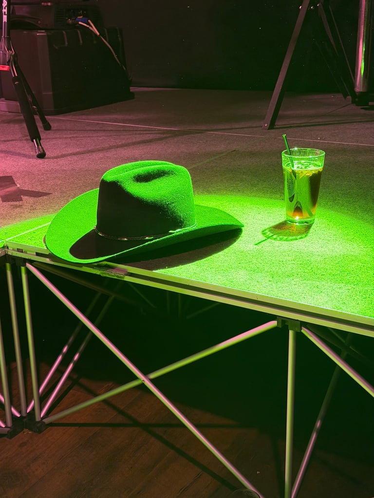 Bright green cowboy hat and glass of whiskey on illuminated table under neon stage lighting
